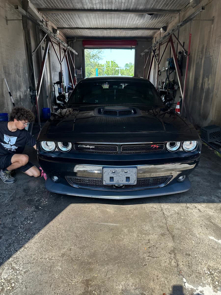 A Wisemen detailer working on a black Dodge Challenger in the wash bay