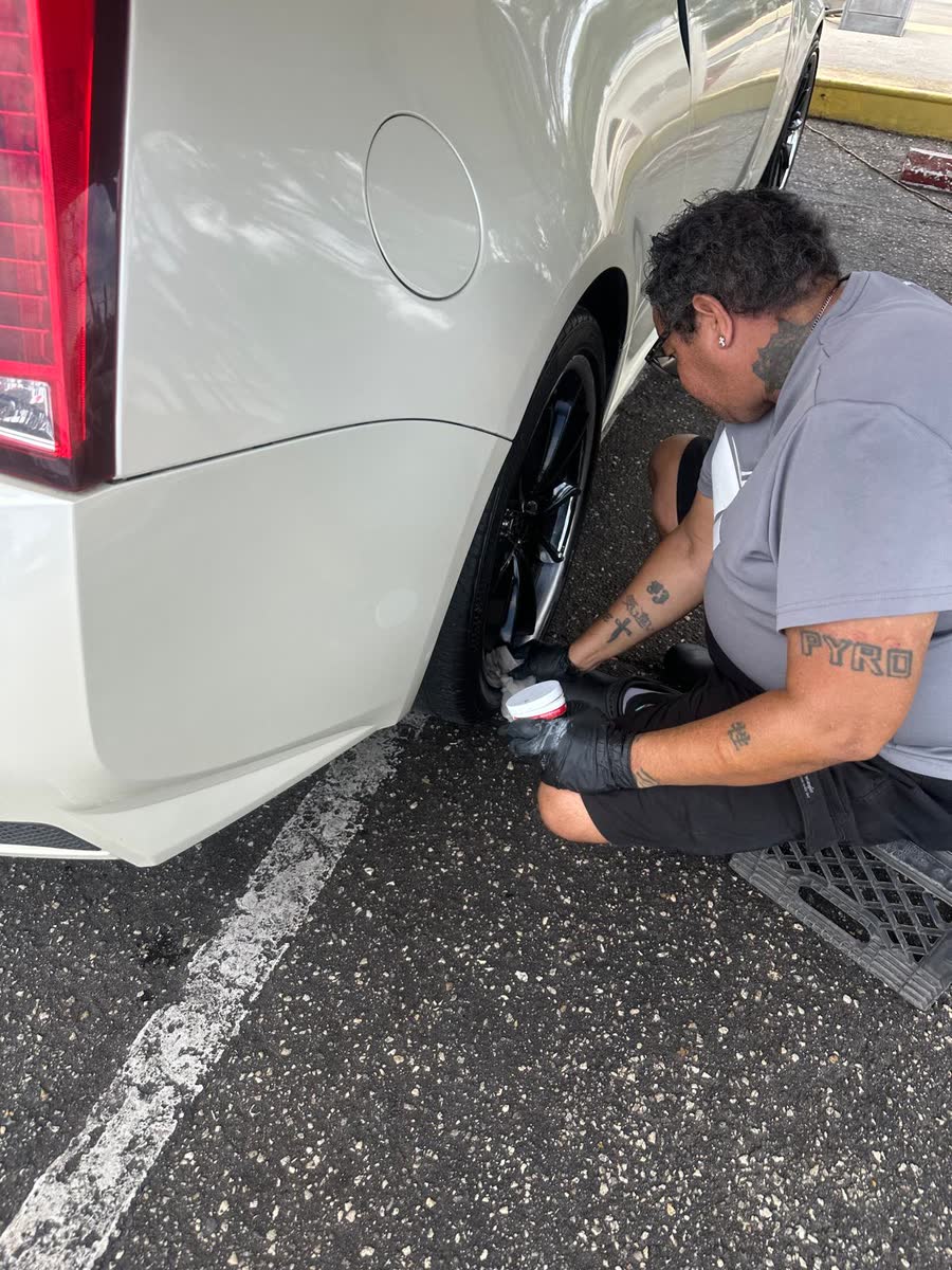 Wisemen detailer cleaning the wheel of a white car by hand